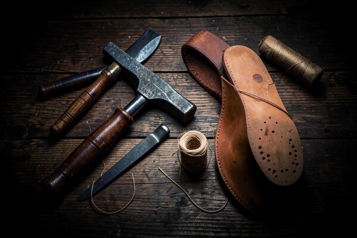 Cobbler hand tools, waxed thread and leather soles laid out on a dark workbench